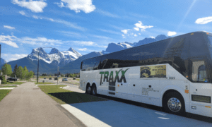 Pro Tours coach bus parked in front of the Rocky Mountains on a clear day during a scenic bus tour from Edmonton.