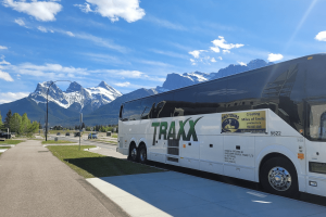 seniors-bus-trips-from-edmonton Pro Tours coach bus parked in front of the Rocky Mountains on a clear day during a scenic bus tour from Edmonton.